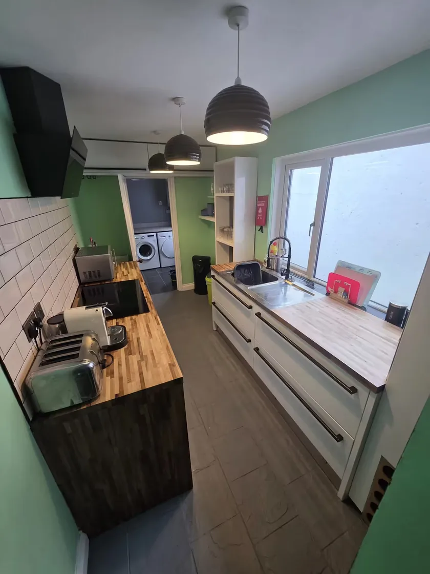 Galley kitchen with white cabinets, wooden worktops and green walls, leading to laundry appliances.