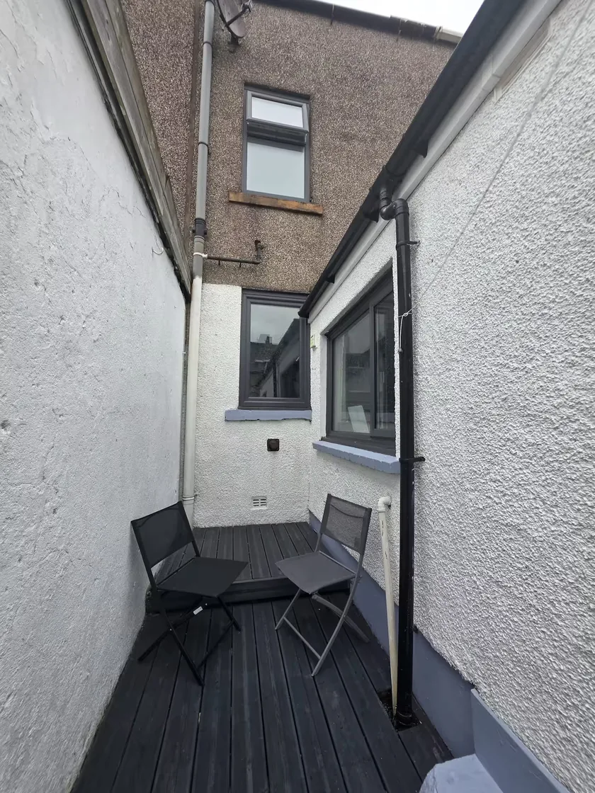 Narrow enclosed rear terrace with decking and two outdoor chairs.