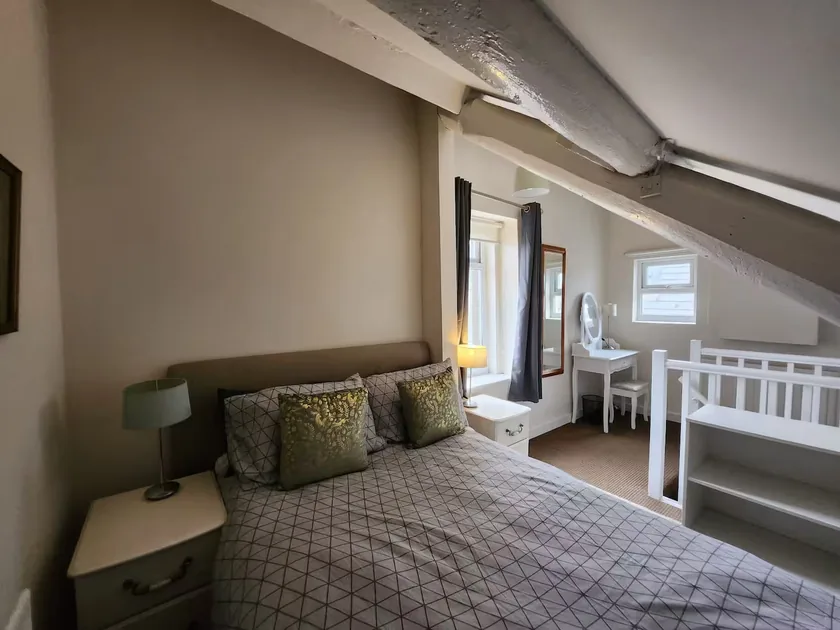 Double bed beneath a sloping ceiling and exposed beam, with windows and a dressing table.