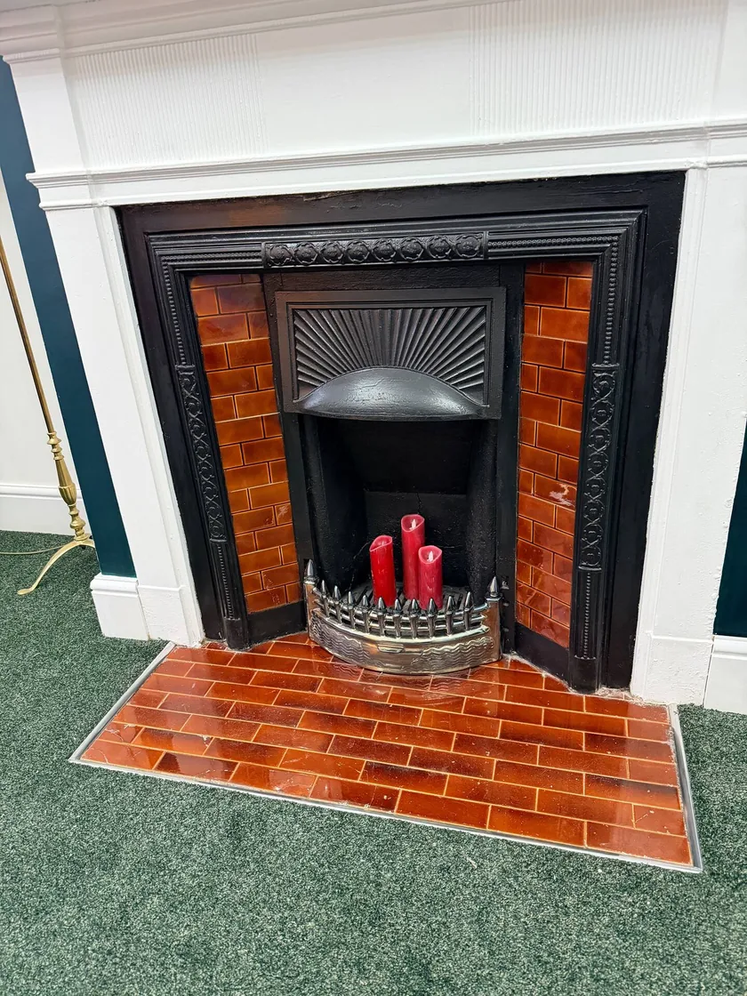 Decorative black fireplace with orange tiles and red candles beneath a white mantel.
