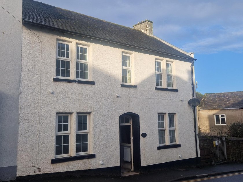 White-painted front of Old Bank Cottage with sash-style windows and a dark doorway.