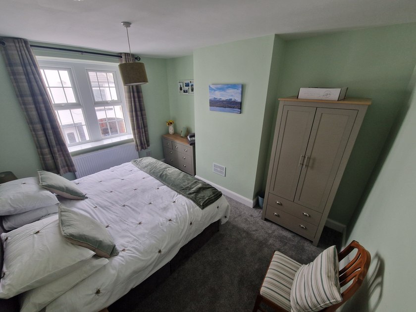 Double bedroom with pale green walls, a grey wardrobe, matching drawers and a cushioned wooden chair.