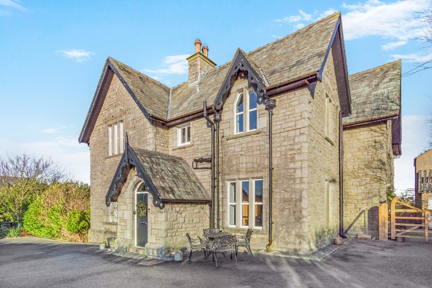 Stone house with gabled slate roofs, a small entrance porch and a table and chairs outside.