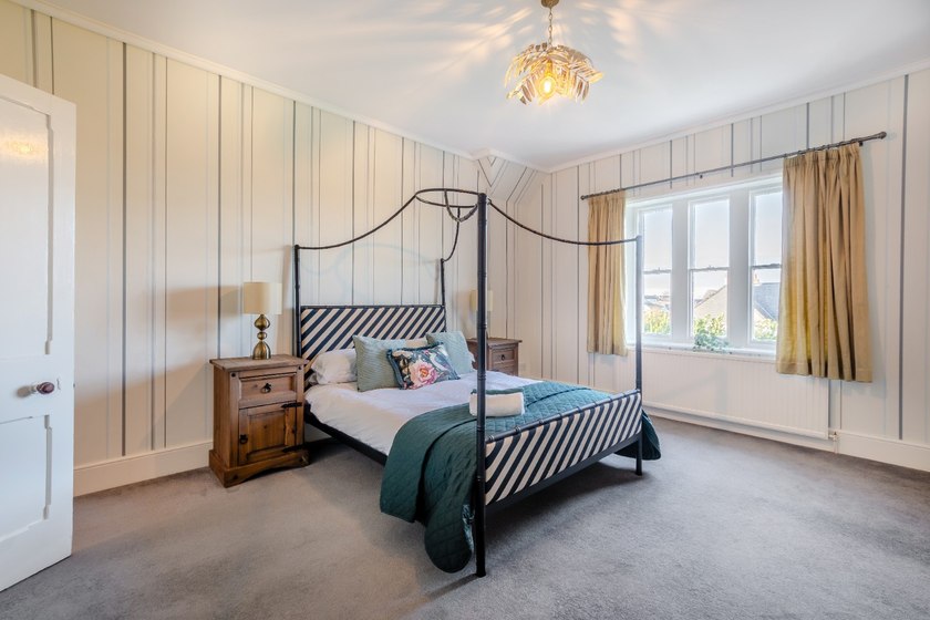 A black metal four-poster bed with striped upholstery and a teal quilt in a room with striped walls and a wide window.