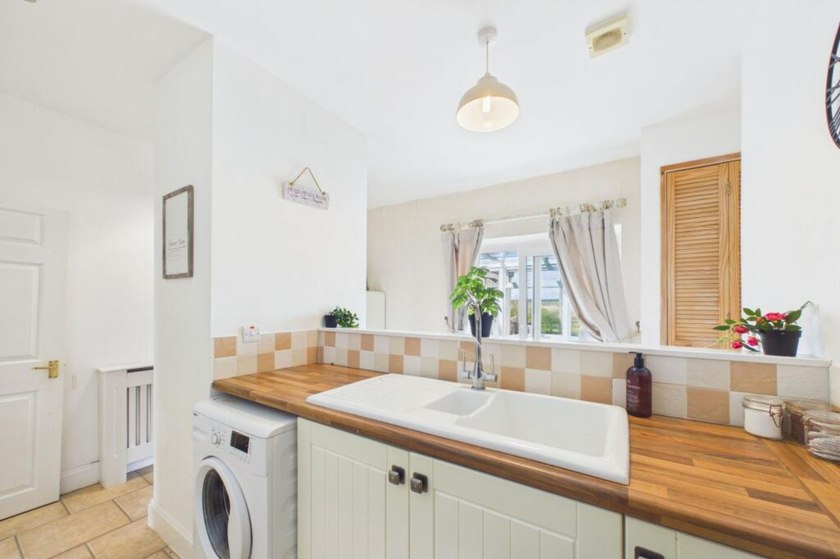 Light kitchen with wooden worktop, white sink and washing machine below.