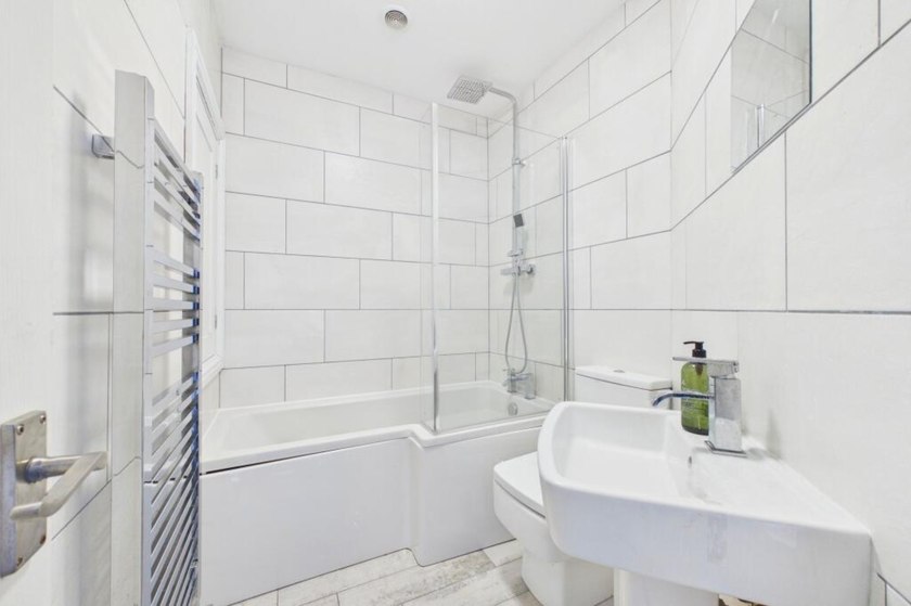 White-tiled bathroom with bath, glass shower screen, basin and heated towel rail.